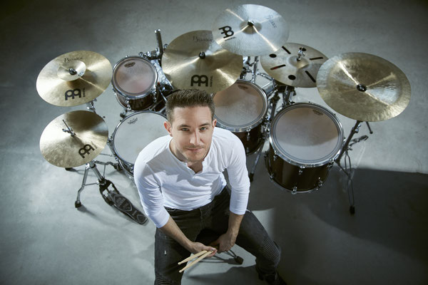 Thomas Sporrer sitzt auf einem Schlagzeughocker. Hinter ihm ist sein Sonor Designer Schlagzeug mit Meinl Becken aufgebaut. 