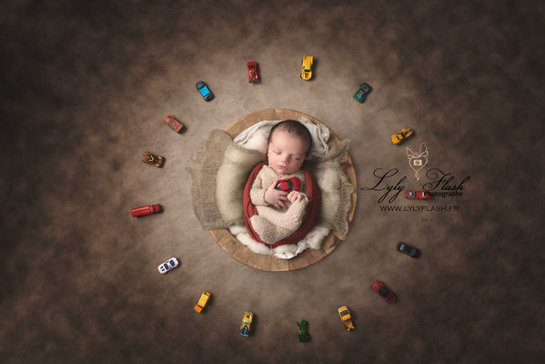 photo de bébé sur le dos dans un contenant en bois avec toutes ses voitures majorettes par Lyly Flash photographe nouveau-né
