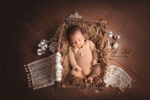 bébé sur le dos avec un pyjama en laine dans un décor en osier et fleurs de coton par Lyly Flash photographe nouveau-né