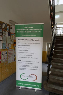 Ein Banner im Treppenhaus mit Informationen zum Netzwerk Gewaltfreie Kommunikation Darmstadt und zum GFK-Tag, den das Netzwerk organisiert.