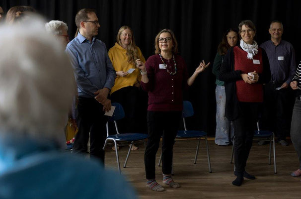 Eine Gruppe von Menschen mit Namenschild am Revers in einer Workshop-Situation auf dem GFK-Tag Darmstadt. In der Mitte steht die GFK-Trainerin Constanze Farzaie.