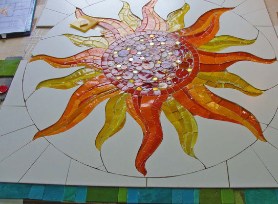 Mosaïque artisanale représentant un soleil flamboyant aux rayons rouges et dorés.