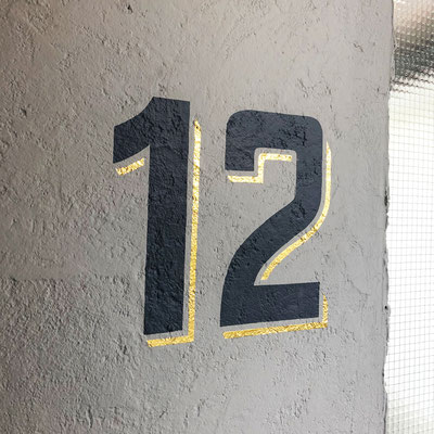 Handgemalte Hausnummer auf Wand von Hauseingang.