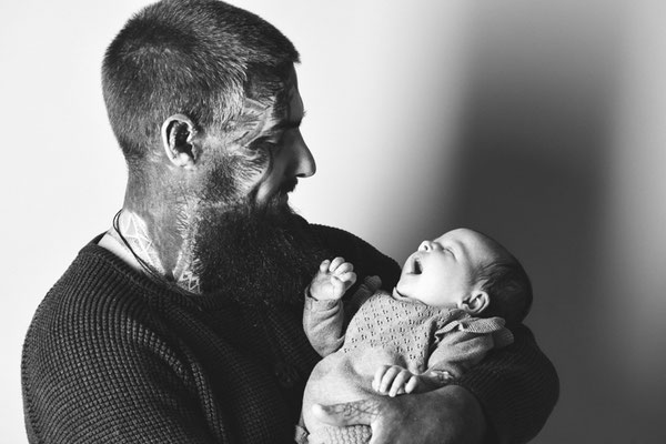 Vater blickt lächelnd auf sein Baby im Arm, schwarzweiße Babyfotografie im Studio in Villach
