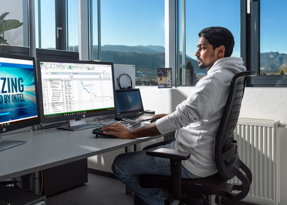 Person bei der Arbeit am Computer in modernem Büro mit mehreren Bildschirmen, Darstellung von konzentrierter digitaler Tätigkeit