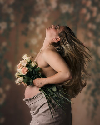 Schwangere Frau hält einen Blumenstrauß, Bewegung im Haar, weiche Studioatmosphäre