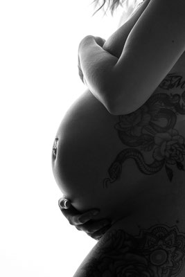 Schwarzweiß-Nahaufnahme eines Babybauchs im Profil, Hände stützen den Bauch im Studio