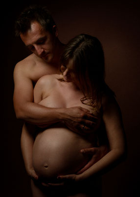 Paar in intimer Umarmung, schwangere Frau hält den Babybauch, stimmungsvolles Licht im Studio