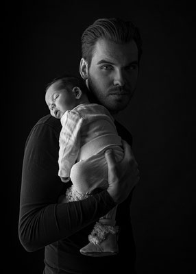Vater trägt sein Baby vor dunklem Hintergrund, Babyfotografie im Studio in Villach