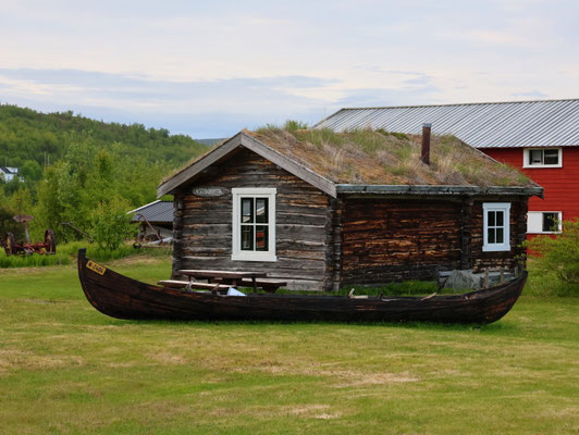 Sehenswürdigkeiten Nuorgam & Utsjoki: Ein traditionell mit Torf isoliertes Holzhaus. Davor liegt eines der Sámi-Boote, mit denen früher Lachse gefangen wurde.