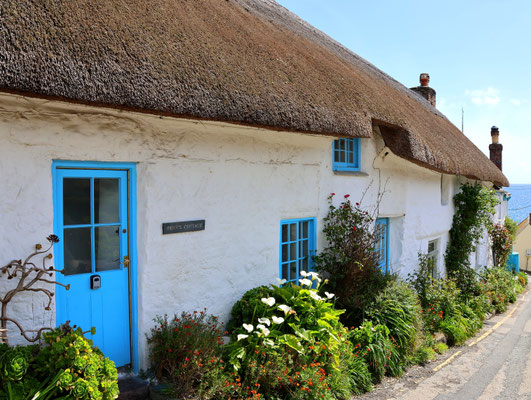Sehenswürdigkeiten Cadgwith: Weiß bemaltes Wohnhaus mit Reetdach und blau bemalter Tür und Fensterrahmen an der Hauptzufuhrstraße zum Dorfkern hin.