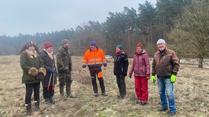 Eine Gruppe von Frauen und Männern in Arbeitskleidung stehen auf einer winterlichen Wiese.