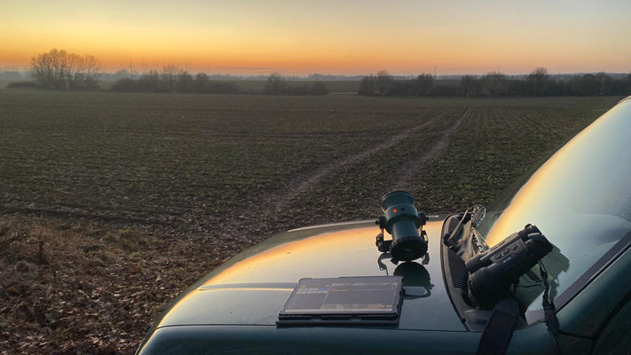 Tablet, Lautsprecher und Fernglas liegen auf einer Motorhaube im Abendlicht.