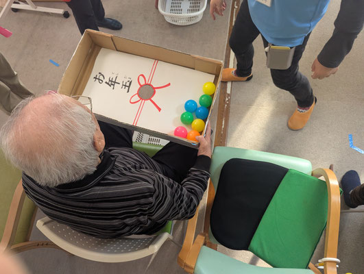 デイサービスの新年会でボールを落とすゲームを楽しむ高齢男性。