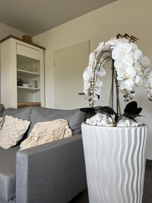 Detailansicht aus dem Wohnzimmer der Ferienwohnung „Auszeit Bergliebe“ mit grauer Couch, gemütlichen Kissen und eleganter Orchidee in einer stilvollen Vase – ein harmonisches Zusammenspiel aus Komfort und geschmackvoller Dekoration.