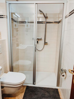 Modernes Badezimmer der Ferienwohnung „Auszeit am See“ mit Dusche, WC und hochwertiger Glaskabine. Helle Fliesen, praktische Ablagen und eine komfortable Ausstattung sorgen für ein angenehmes Frischeerlebnis während des Aufenthalts.