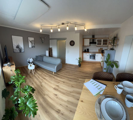 Offener Wohnbereich der Ferienwohnung „Auszeit Winterberg“ in Niedersfeld mit moderner Einbauküche, gemütlicher Sitzecke, stilvoller Dekoration und hellem Holzfußboden. Eine einladende Kombination aus Komfort und Design im Sauerland.