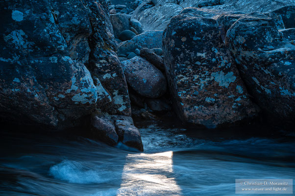 Das letzte Sonnenlicht fällt auf das Wasser zwischen zwei Steinen