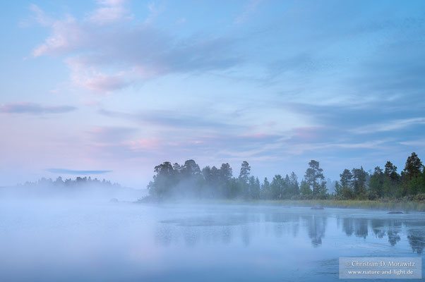 In der zeitigen Morgendämmerung liegt Nebel über dem Inari-See