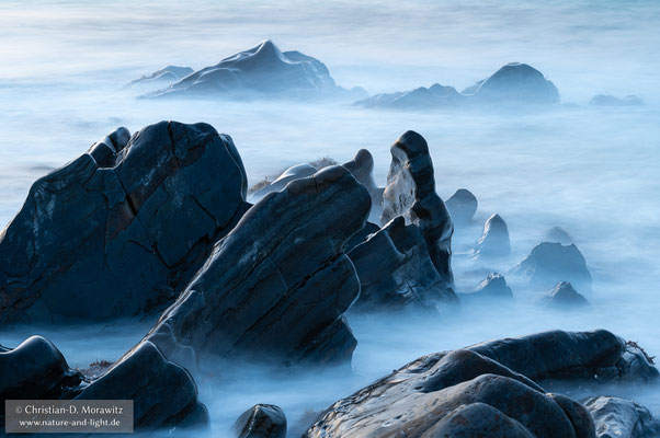 Die Wellen brechen sich an den schroffen Steinen der Küste