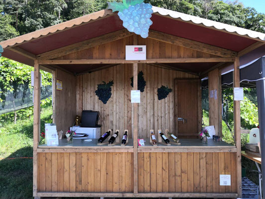 Ein offenes Messe-Häuschen aus Holz, auf welchem sechs Weinflaschen präsentiert werden