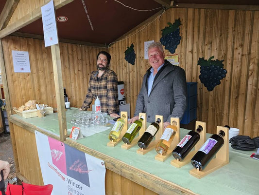 Zwei Männer stehen in einem Markthäuschen und verkaufen Wein