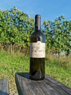 Eine Weinflasche Chardonnay steht auf einem Holzstück vor den Reben