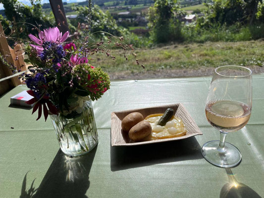 Auf einem Tisch steht ein Weinglas mit Weisswein, eine Portion Raclette und eine Vase mit frischen Blumen