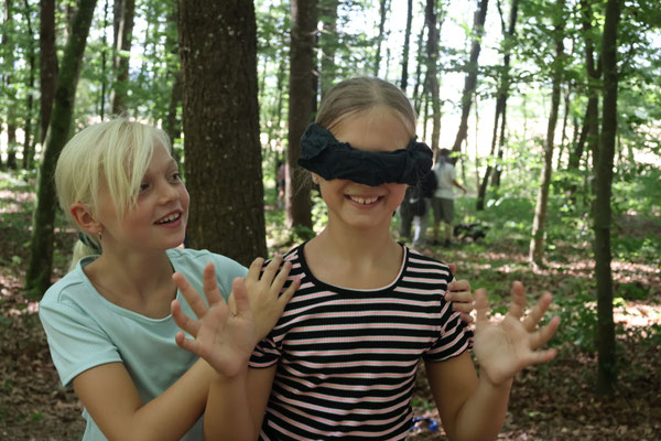 Ein Mädchen wird mit verbundenen Augen durch den Wald geführt