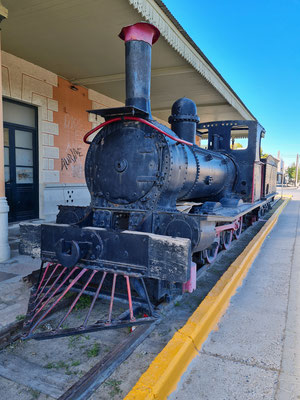 Stillgelegte Lokomotive hinter dem Bahnhofsgebäude