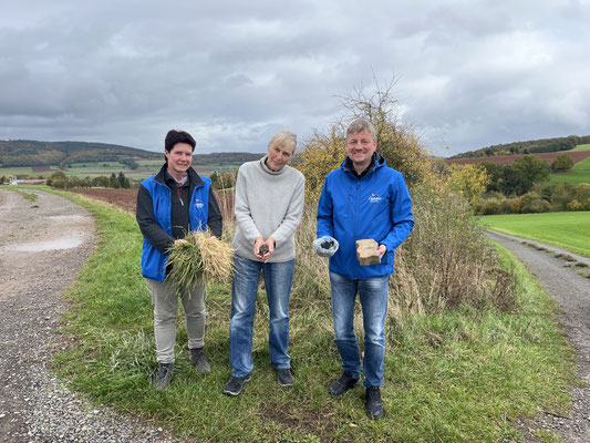 v. l. n. r: Erika Höhle, Angela Odenhardt und Markus Jungermann halten die Ausgangs- und Endprodukte der Grasverarbeitung in den Händen: Gras, Graspellets, Pflanzenkohle und ein Beton-Pflasterstein.