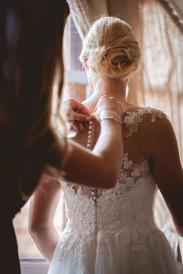 Die Trauzeugin macht das Brautkleid zu.