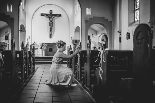 Die letzten Vorbereitungen in der Kirche. Frau bringt Blumenschmuck an Kirchenbank an.