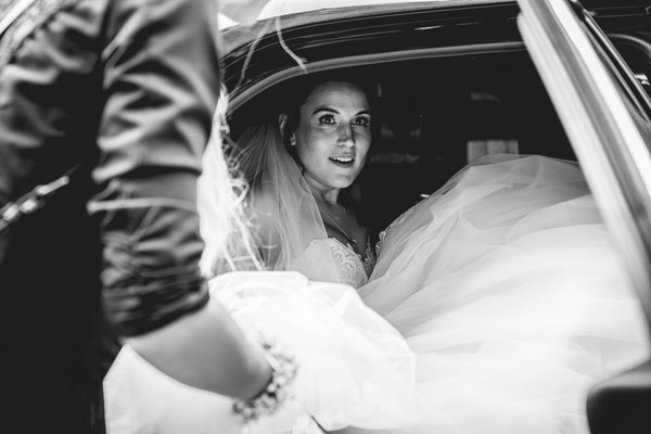 Braut sitzt im Auto mit viel Kleid.