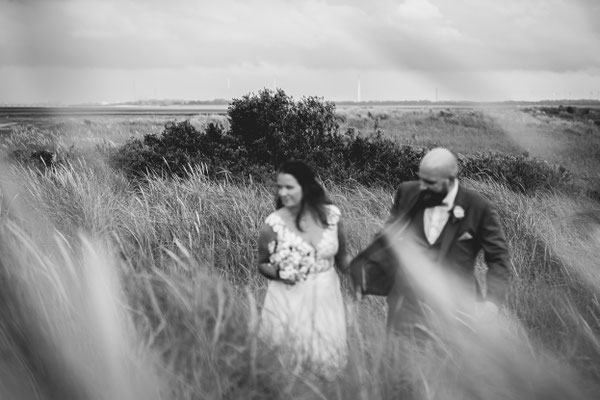 Brautpaar läuft, Hand in Hand, durch die Dünen in Hooksiel an der Nordsee.