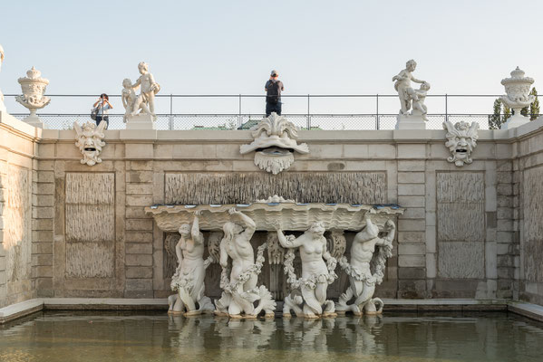 Muschelbrunnen, In der Mitte befindet sich eine Tritonengruppe ein Muschelbecken haltend, darüber wasserspeiende Masken. (dzt. außer Betrieb.) An der oberen Kante und der Rampe sind Ziervasen und Puttengruppen.