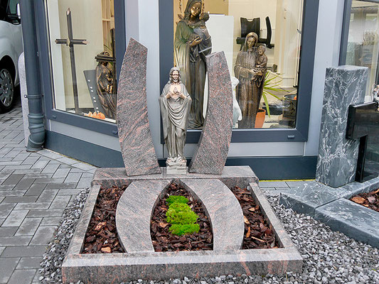 Urnengrab mit gebogenen Säulen, die sich auf der Grabfläche wiederspiegeln. Mittig eine Madonna aus Bronze