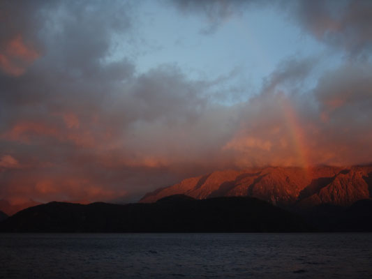 Die Sonne erreicht die Berge und lockt einen Regenbogen hervor