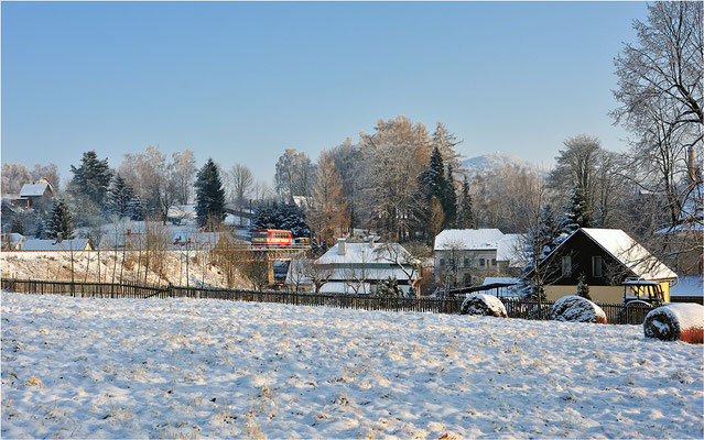 Auf der ehemaligen Nordböhmischen Industriebahn rumpelt 810 165-1 über eine kleine Stahlträgerbrücke in Staré Krecany (Alt Ehrenberg) im Ortsteil Brtníky (Zeidler). Im Hintergrund erhebt sich der 581m hohe Vlcí hora (Wolfsberg). 26.01.2014