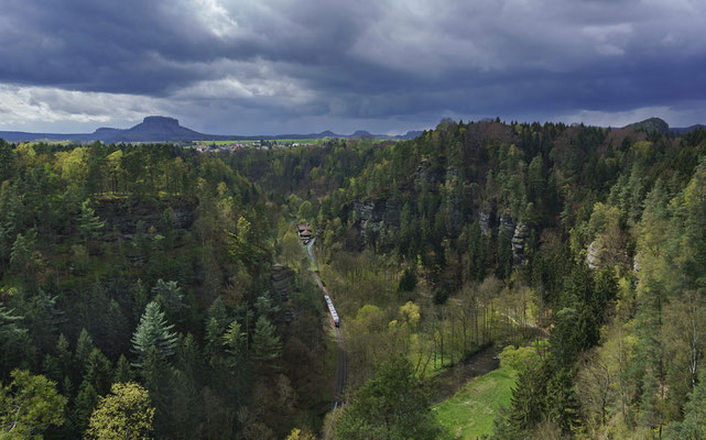 Blick ins Sebnitztal von den Ochelwänden. Im Tal ist ein Zug der Nationalparkbahn unterwegs von Bad Schandau nach Rumburk in Tschechien. 