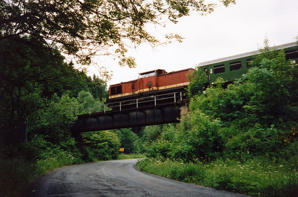 Ein Zug mit der 112 063-3 überquert von Sebnitz kommend kurz nach dem Haltepunkt Amtshainersdorf die Straße (nach Ulbersdorf) und den Sebnitzbach, um gleich darauf in den Tunnel 2 zu verschwinden, 1991. Text & Foto: Archiv Axel Förster.