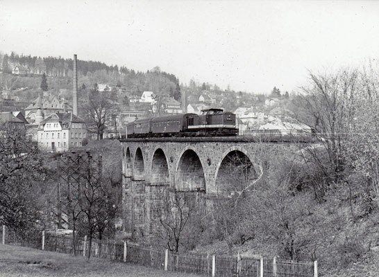 Eine typische Reichsbahngarnitur der 80ér Jahre mit V100 und Reko 4-Achsern unterwegs von Bautzen nach Bad Schandau auf dem Sebnitzer Stadtviadukt. Auch hier zu erkennen: Erste Stützelemente der Behelfsbrücke. 1984, Foto: Archiv Sven Kasperzek.