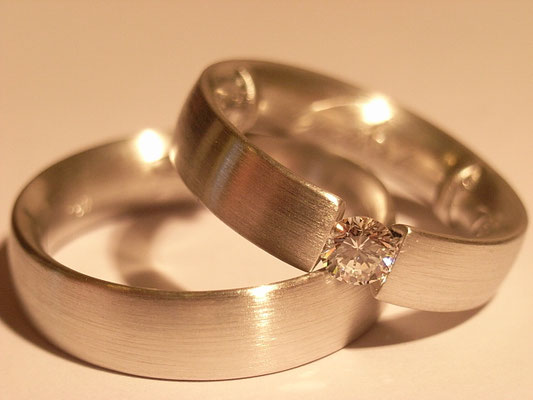 Weißgoldspannring mit weißem Brillanten als Damenring, der Herrenring klassisch schlicht.