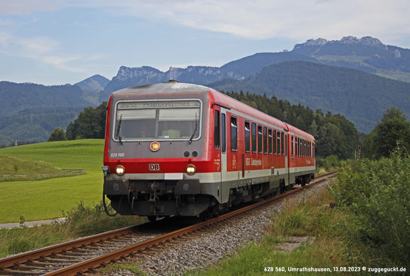 628 560 ist am 13. August 2023 für den Dienst auf der Chiemgaubahn eingeteilt. Hier fährt er vor der Kulisse der Kampenwand gleich am ehemaligen Empfangsgebäude von "Umrathshausen Bahnhof" vorbei.