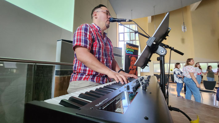 Nahaufnahme von Hanjo: Er singt und spielt Klavier, während der Chor den Segen zwischen den Gästen singt.