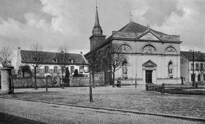 1904 Kirche mit Brunnen Straßen im Vordergrund gepflastert, Marktfläche Schotter. Vorne links eine Litfaßsäule