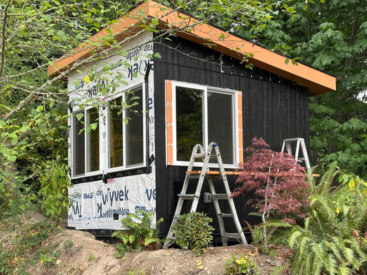 August 5, 2025. Installing the triangular panels above the 4' x 8' panels with "Z" flashing, and also beginning to install the painted trim around the first window.