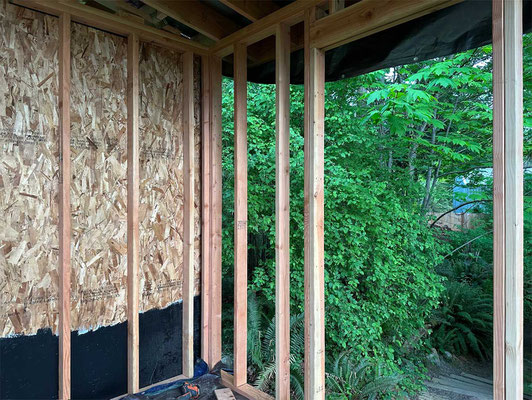 May 11, 2025. The first OSB sheathing goes up, applied to the wall without windows. I pre-painted each sheathing panel with two coats of primer and two coats of paint, including all edges and 18 inches on the backsides.