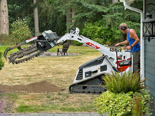 July 9, 2025. Eric Conzelmann using a rented trencher to dig a 100-foot trench from our house to the studio, where electrical wiring will be laid in conduit.