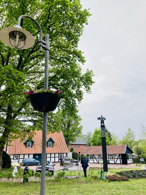 Vor dem Dorfplatz ziert ein bepflanzter Blumenkasten eine Laterne.